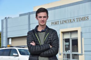Mitchell Paterson, a young white man, stands outside the office of the Port Lincoln Times. He is wearing a black leather jacket and grey shirt, and has his arms folded. He has short dark hair.