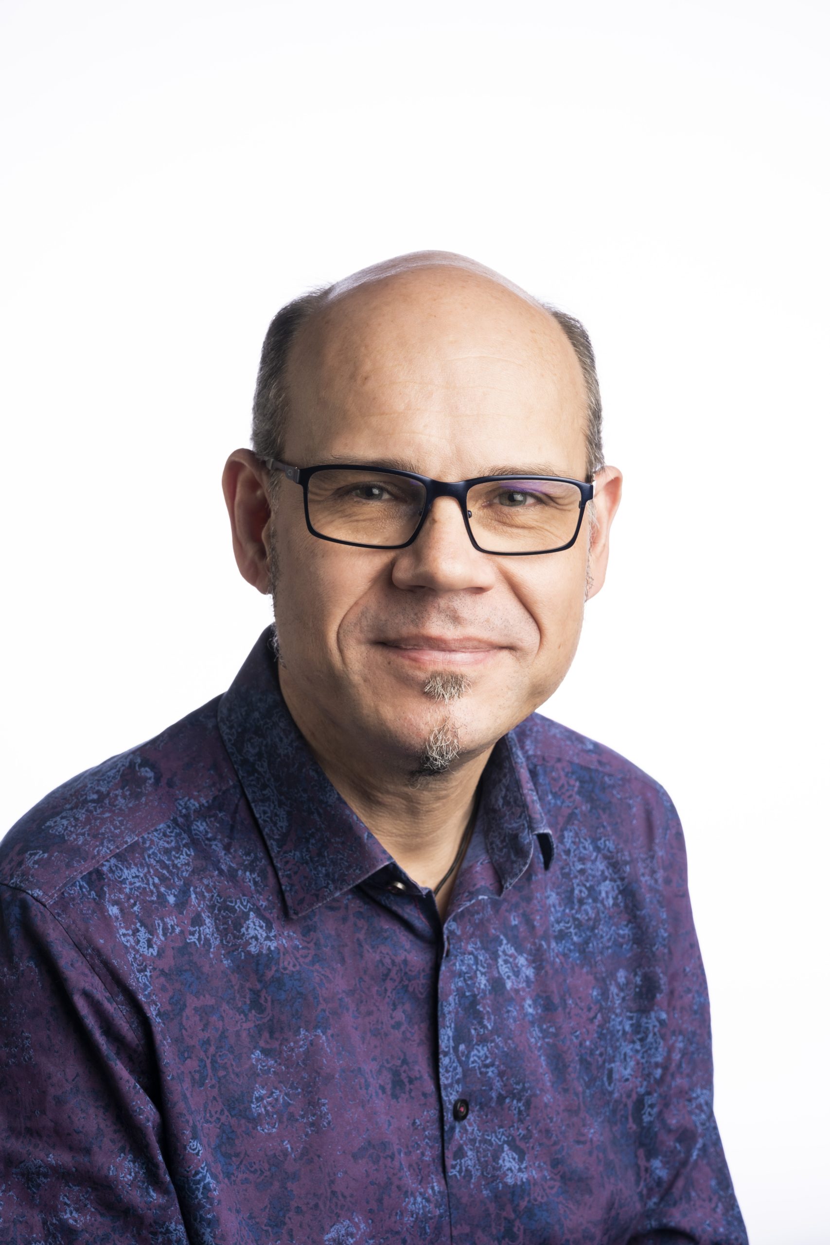 A head shot of Axel Bruns. He is wearing a colourful purple and blue button-up shirt, and wears black-rimmed glasses. He is bald.
