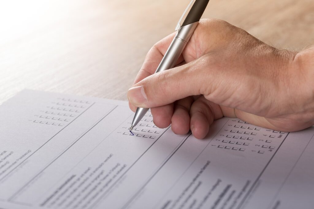 A person filling out a survey on a piece of paper with a black pen.