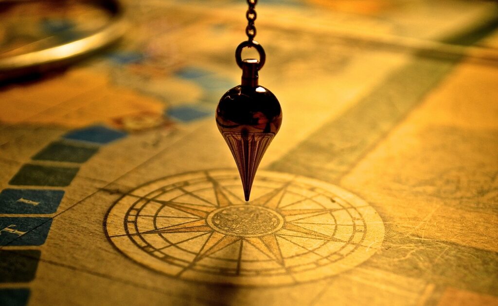 An image of a flat, golden compass, with a pointed pendulum hanging over it.
