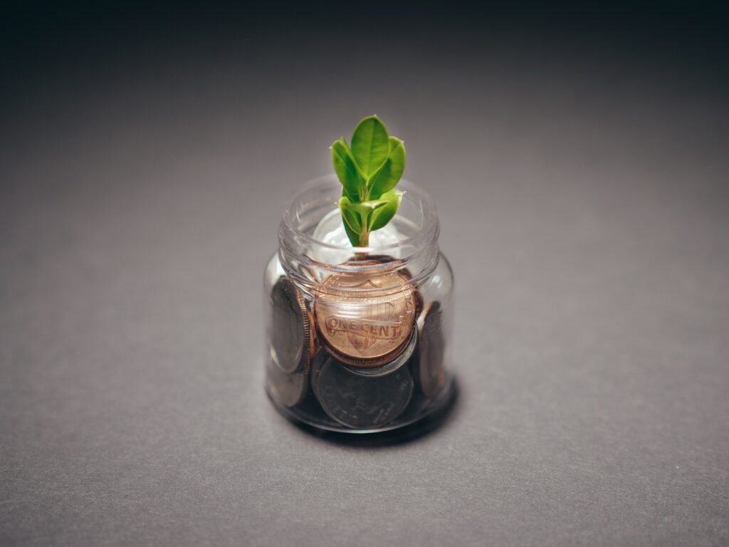 A small jar of coins with a green plant growing out the top.