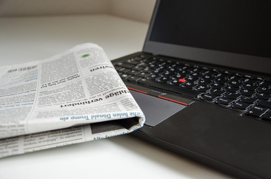 A folded newspaper lies on top of an open black laptop.