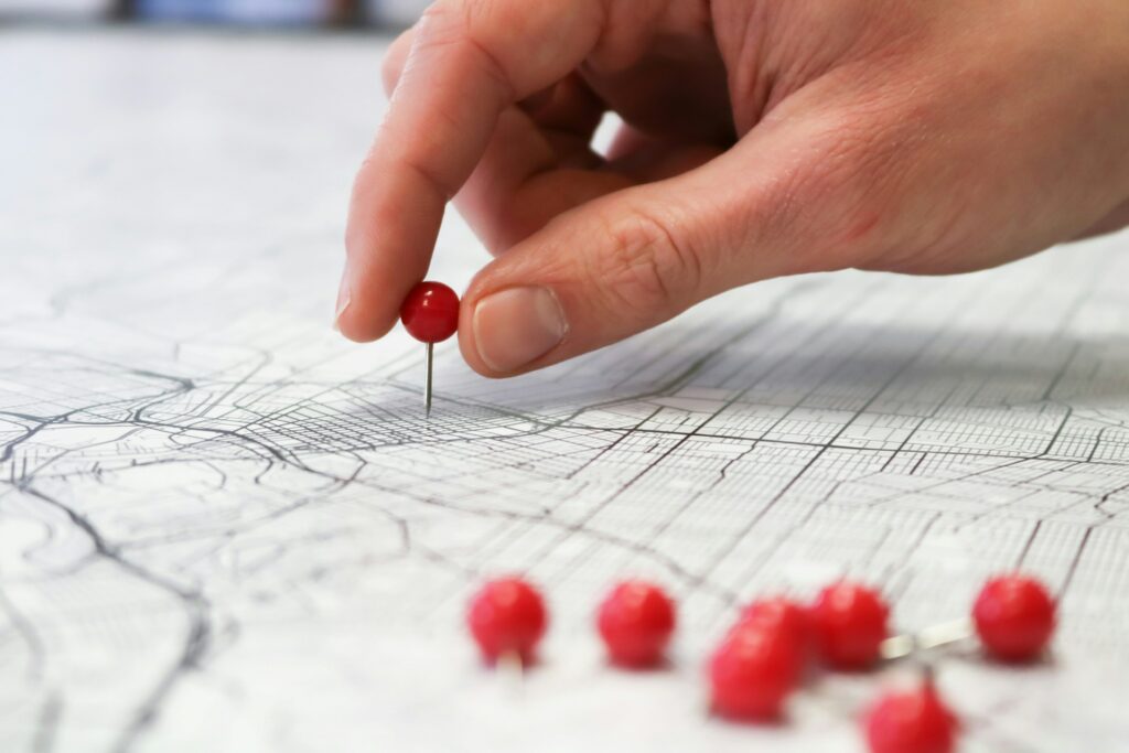 A hand pushing red push pins into a map with lines on it.